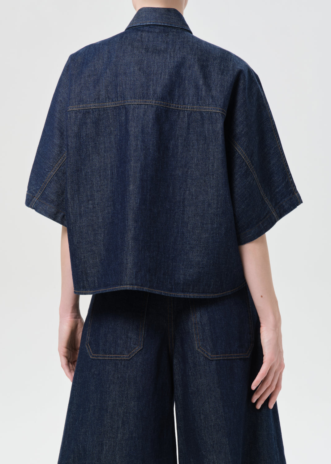 Person wearing a dark blue denim shirt and pants on a white background