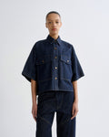 Person wearing a dark blue denim jacket and pants on a white background