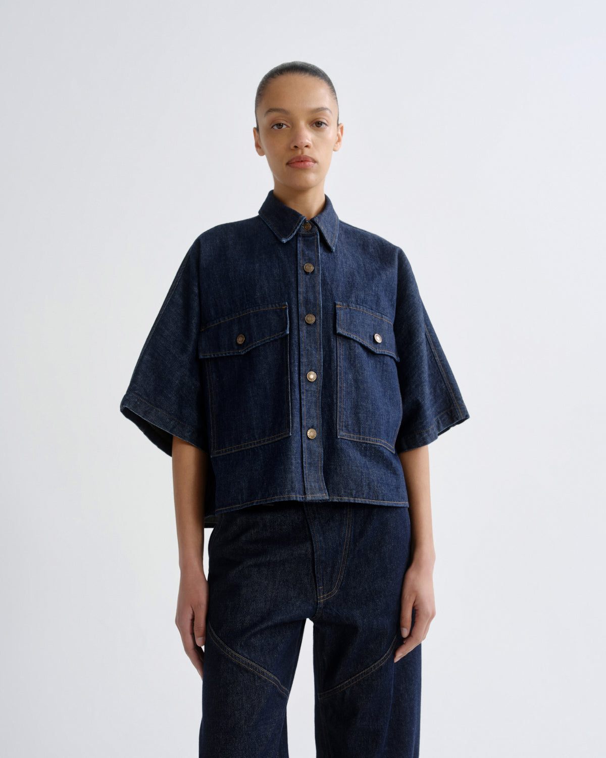 Person wearing a dark blue denim jacket and pants on a white background