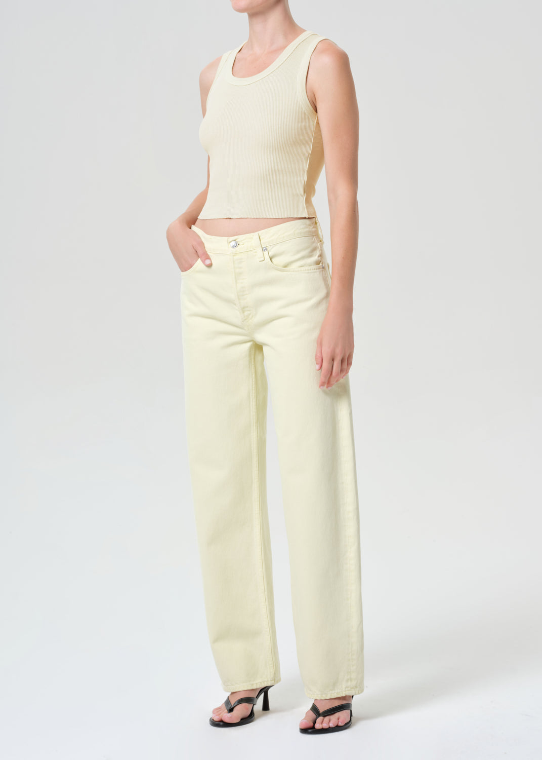 Person wearing a light yellow sleeveless top and high-waisted pants on a white background
