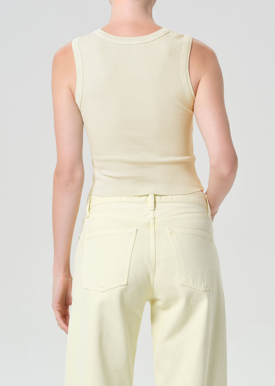 Person wearing a light yellow sleeveless top and pants on a plain background