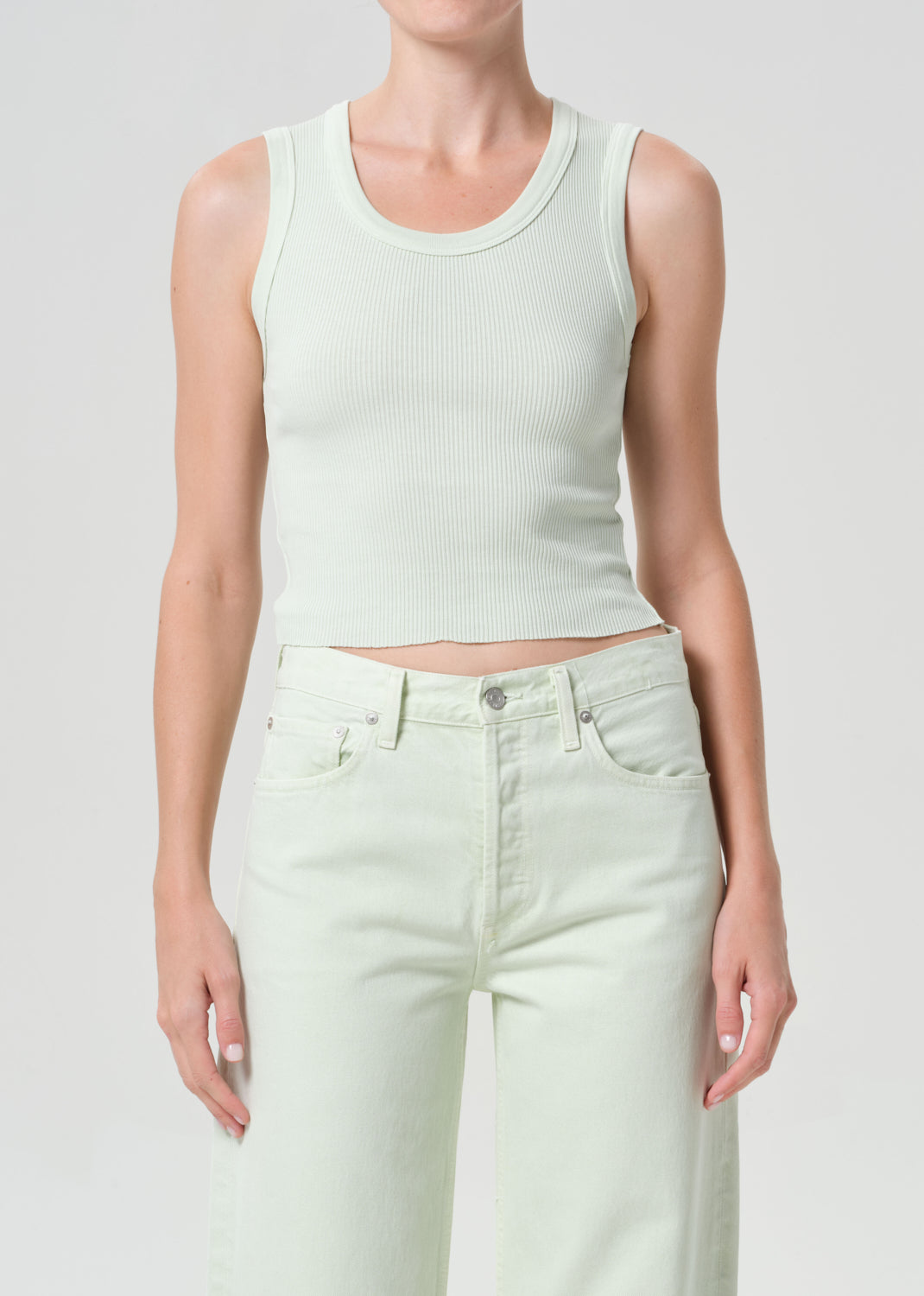 Person wearing a light green tank top and pants on a plain background