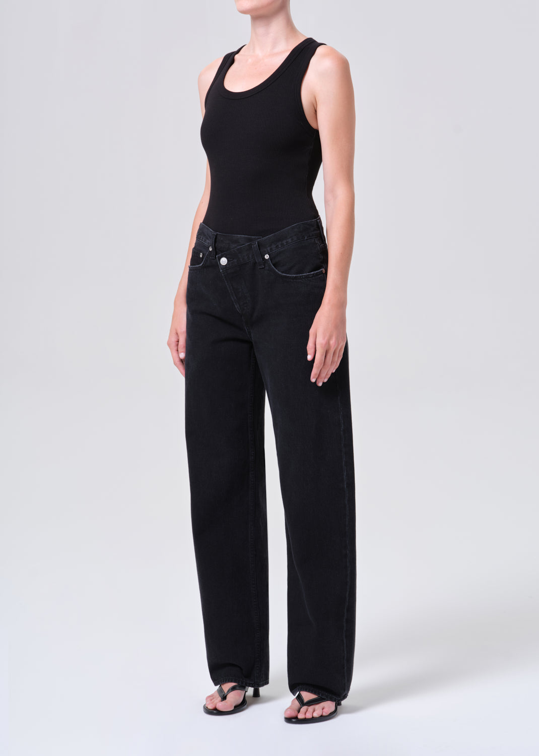 Person wearing a black sleeveless top and black jeans on a white background