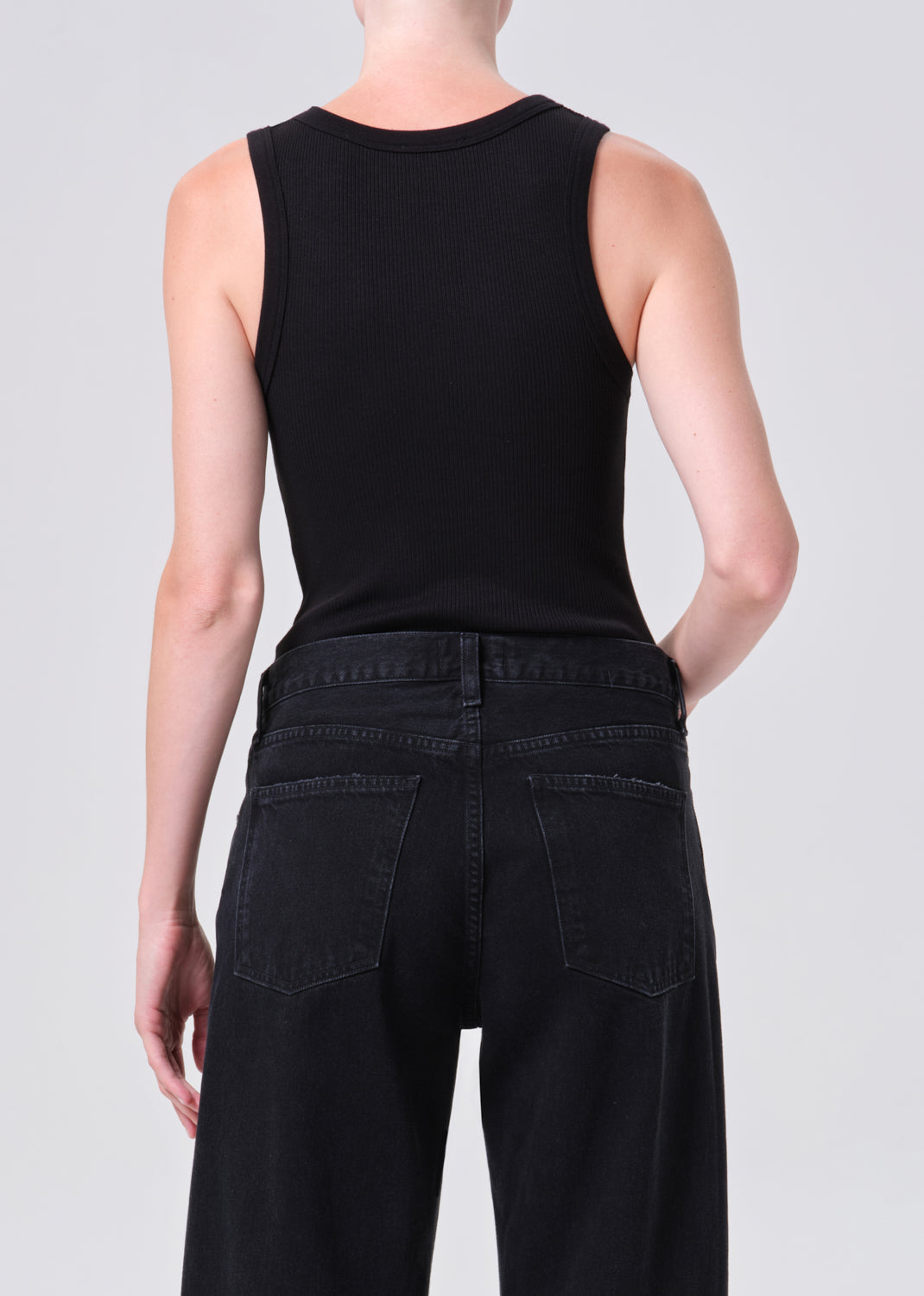 Person wearing a black sleeveless top and black pants on a light gray background
