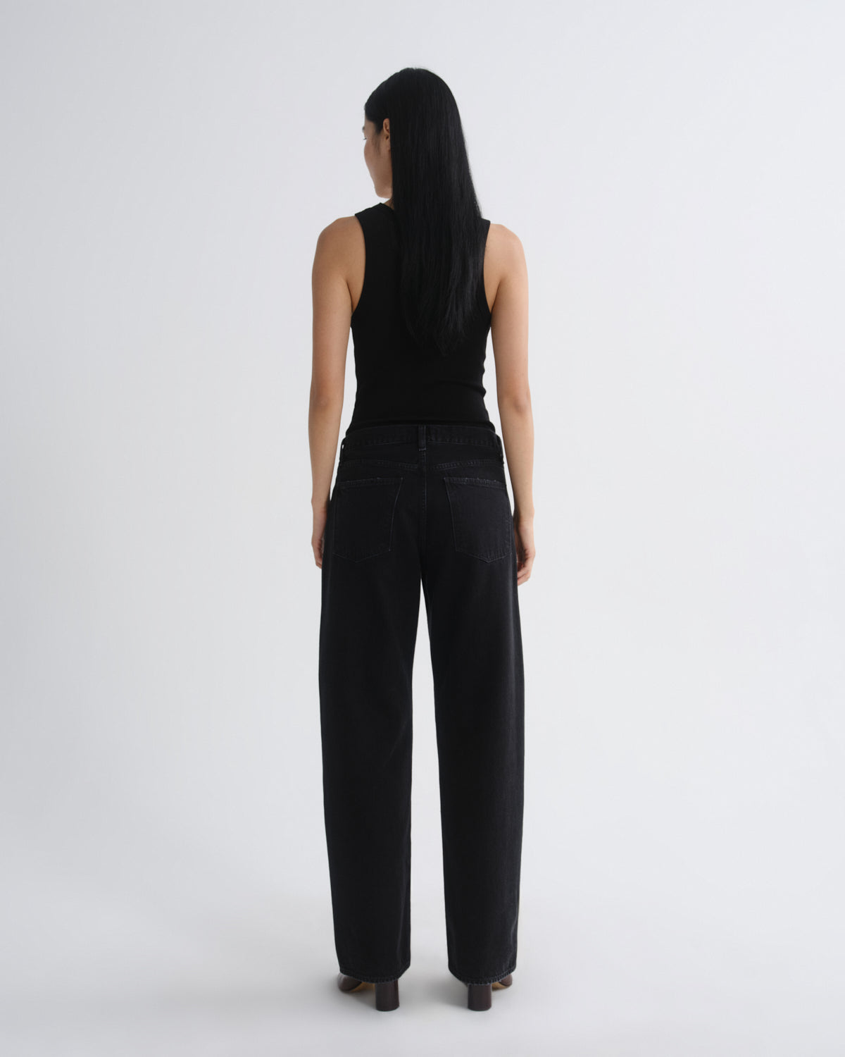 A model viewed from the back wearing a black sleeveless top and black wide-leg jeans against a plain light gray studio background.