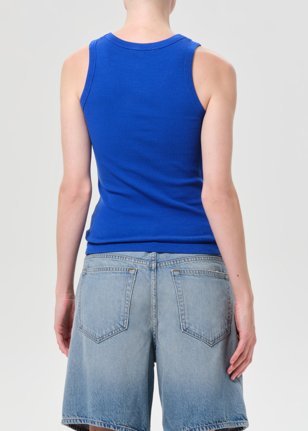 Person wearing a blue tank top and light blue denim shorts on a plain background