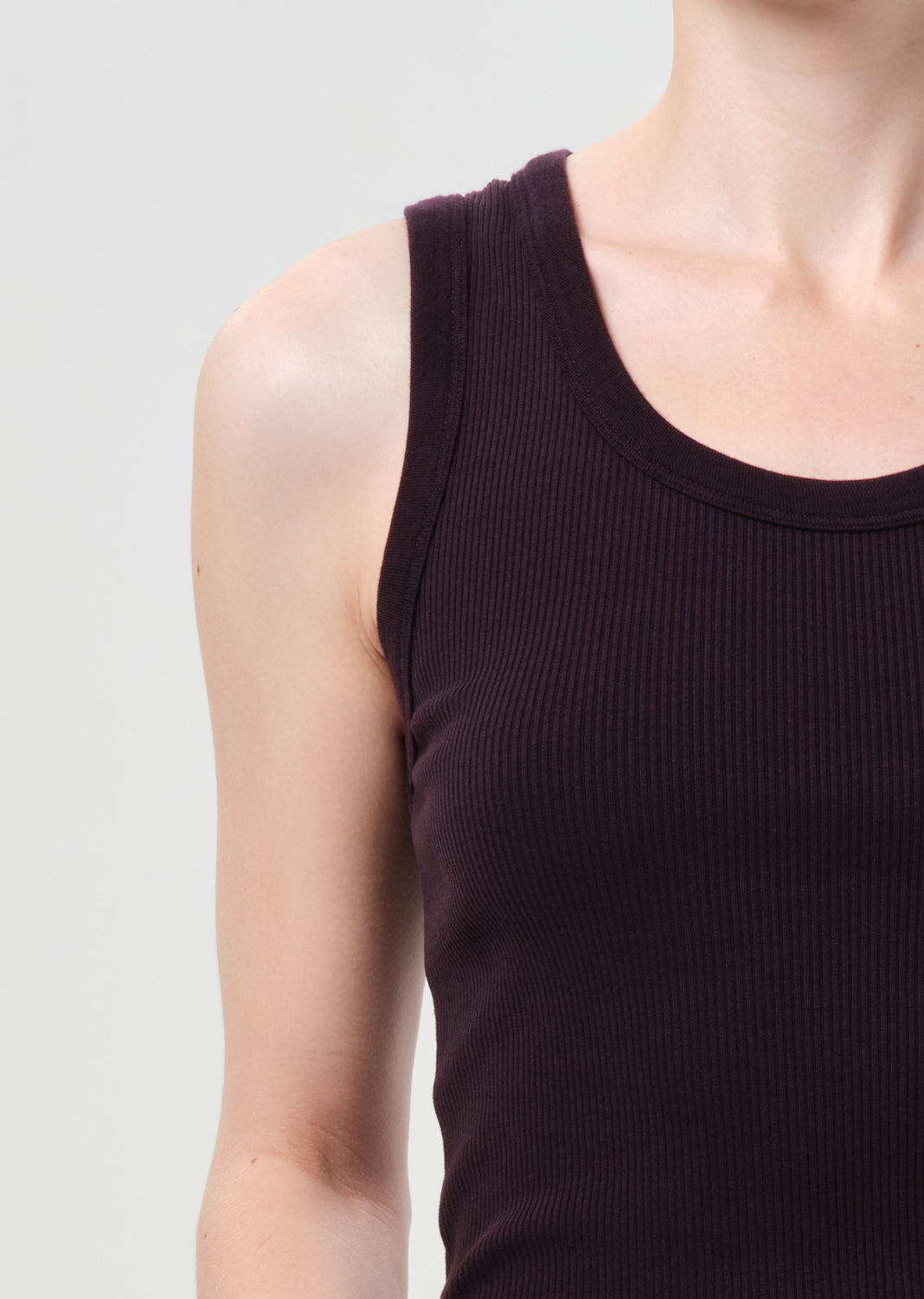 Close-up of a person wearing a dark brown ribbed tank top against a light gray background