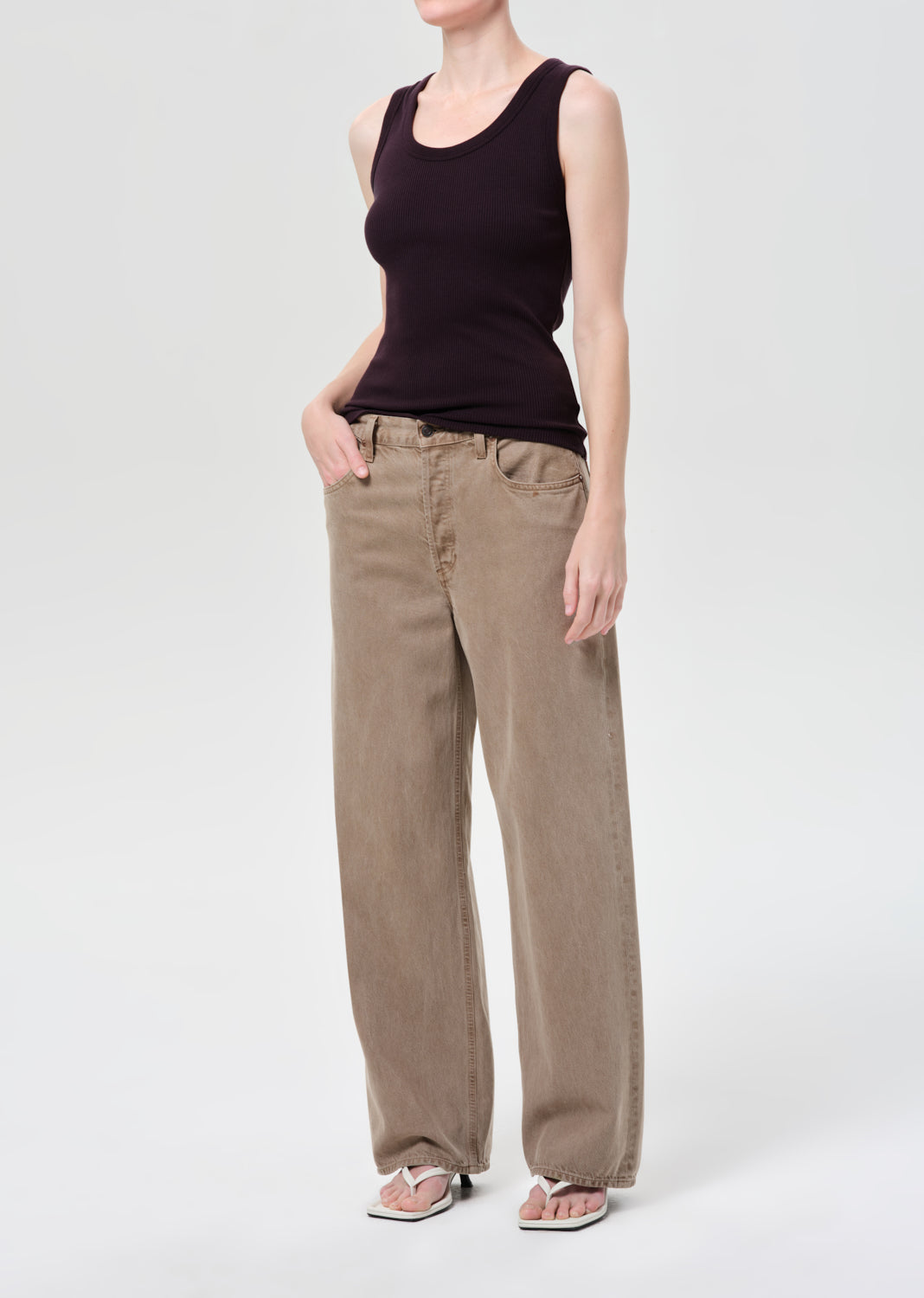 Person wearing a black tank top and beige pants on a white background