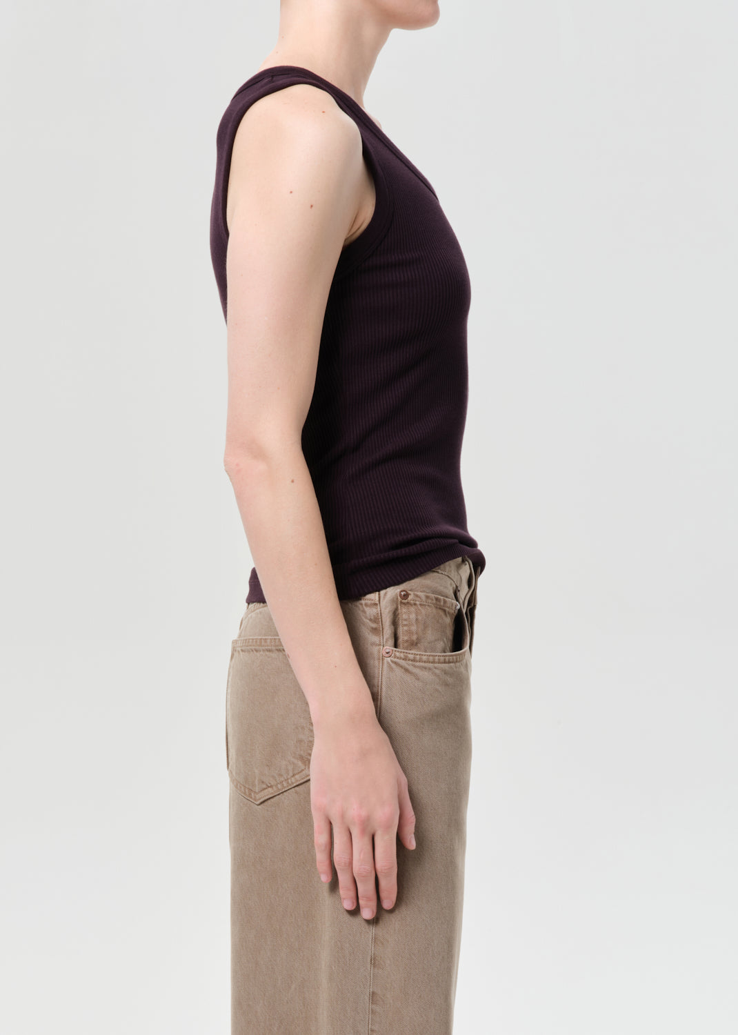 Person wearing a dark purple sleeveless top and beige pants on a light gray background