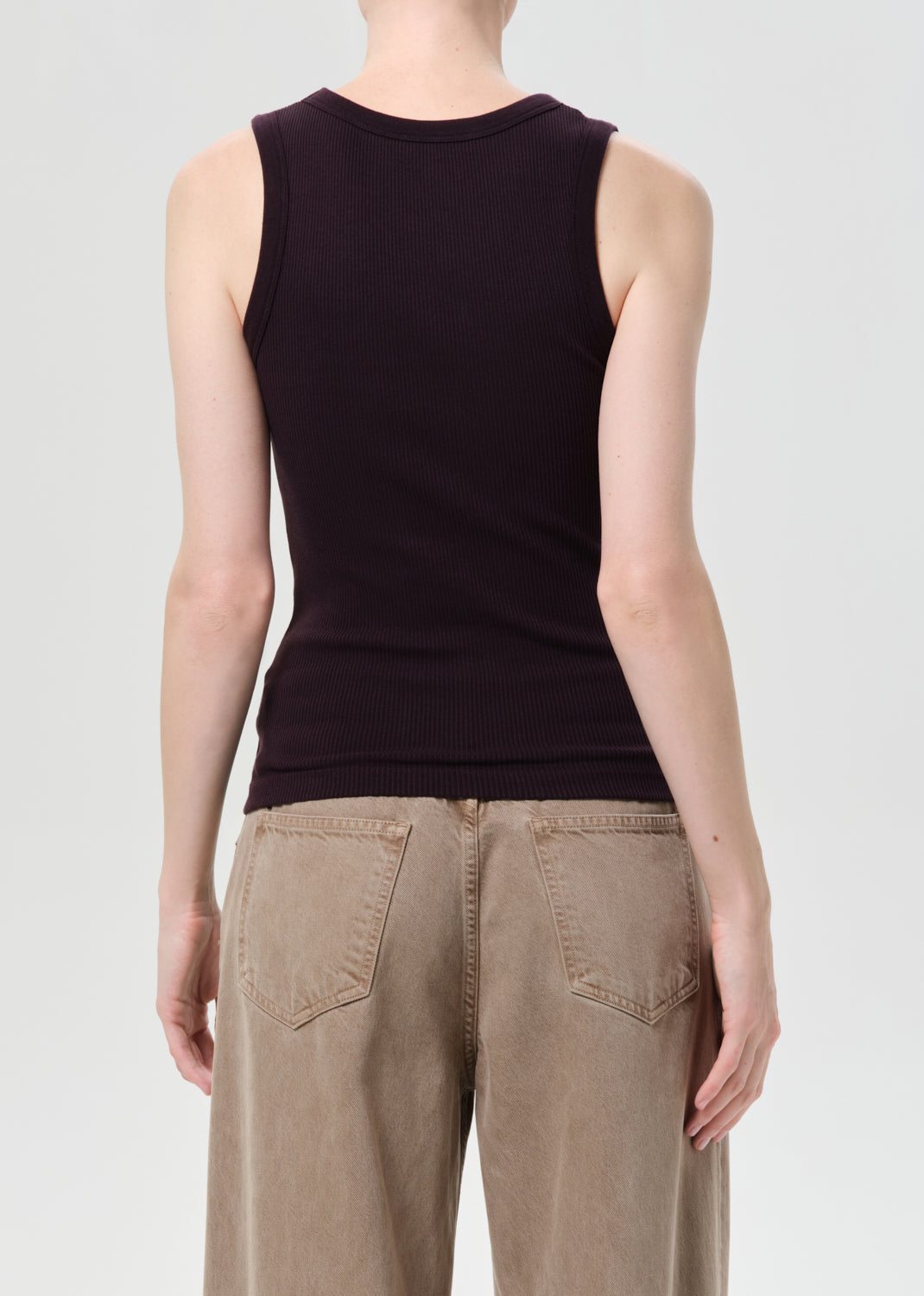 Person wearing a black sleeveless top and beige pants on a light gray background
