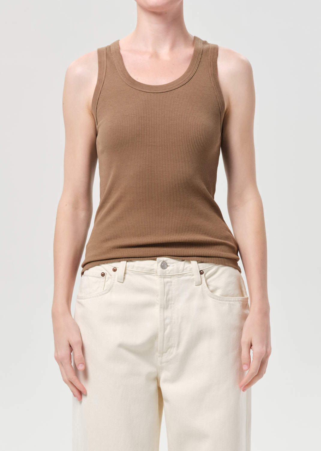 Person wearing a brown tank top and white pants on a plain background