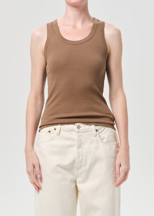 Person wearing a brown tank top and white pants on a plain background