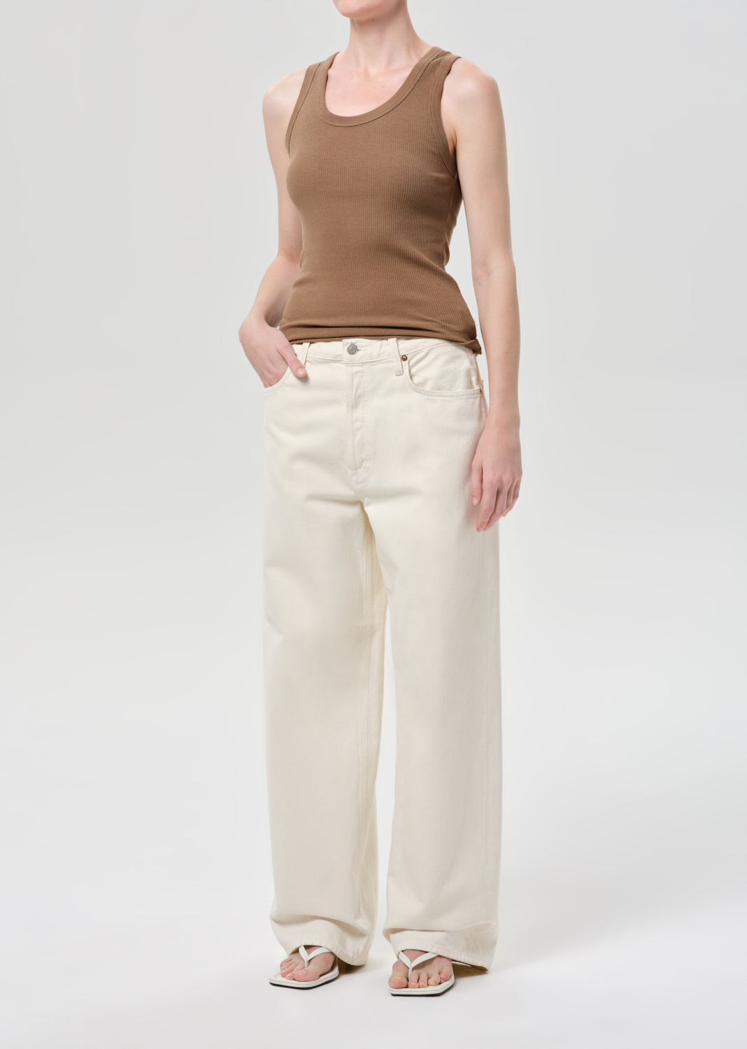 Person wearing a brown tank top and white pants on a white background