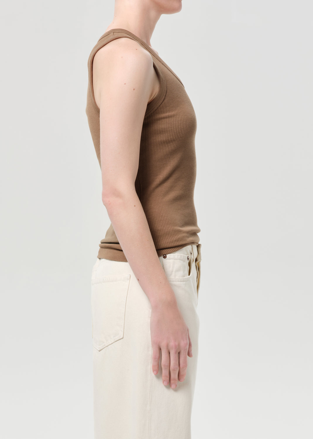 Person wearing a brown tank top and beige pants on a light gray background