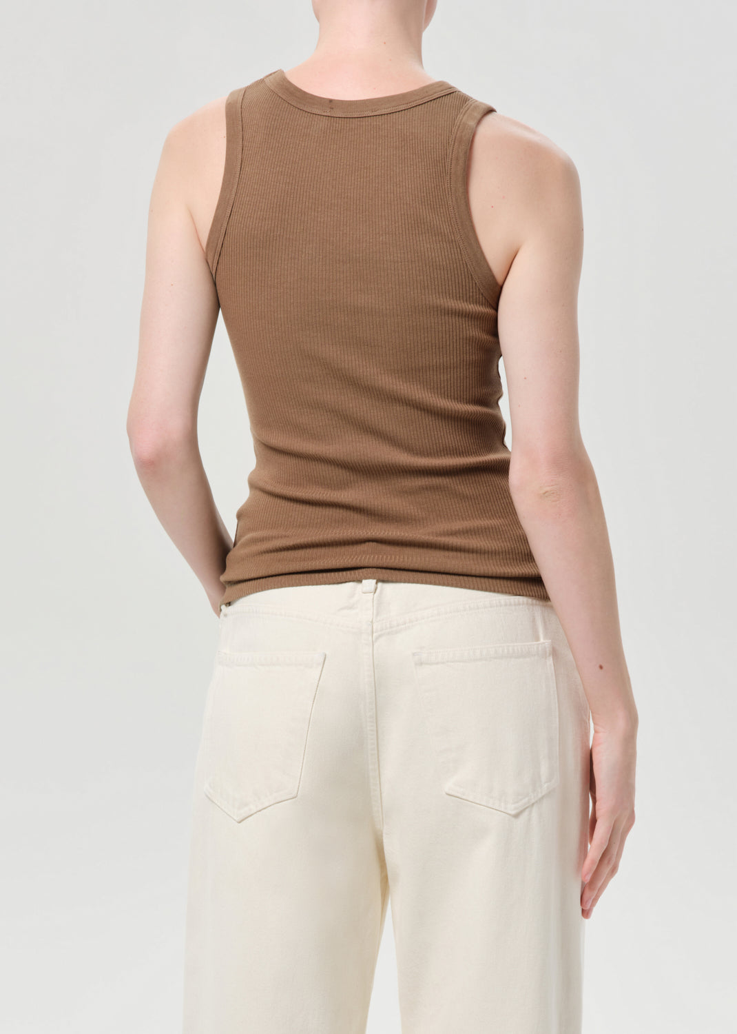 Person wearing a brown tank top and white pants on a plain background