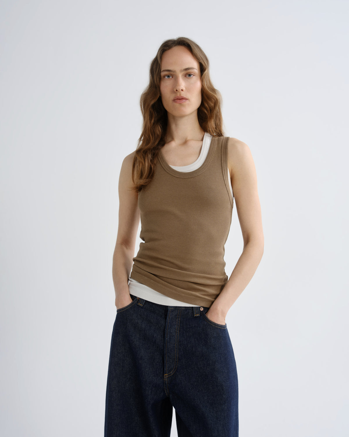 Woman wearing a brown tank top and dark pants on a white background