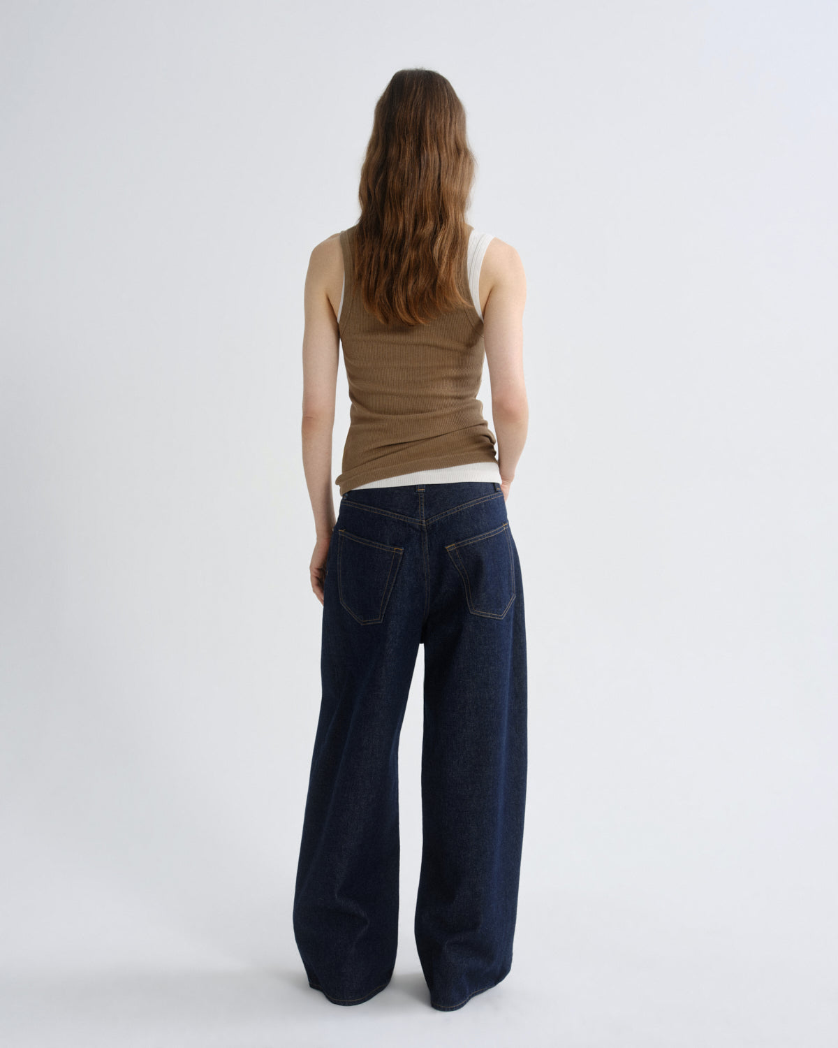 Woman wearing a brown tank top and dark blue jeans on a white background