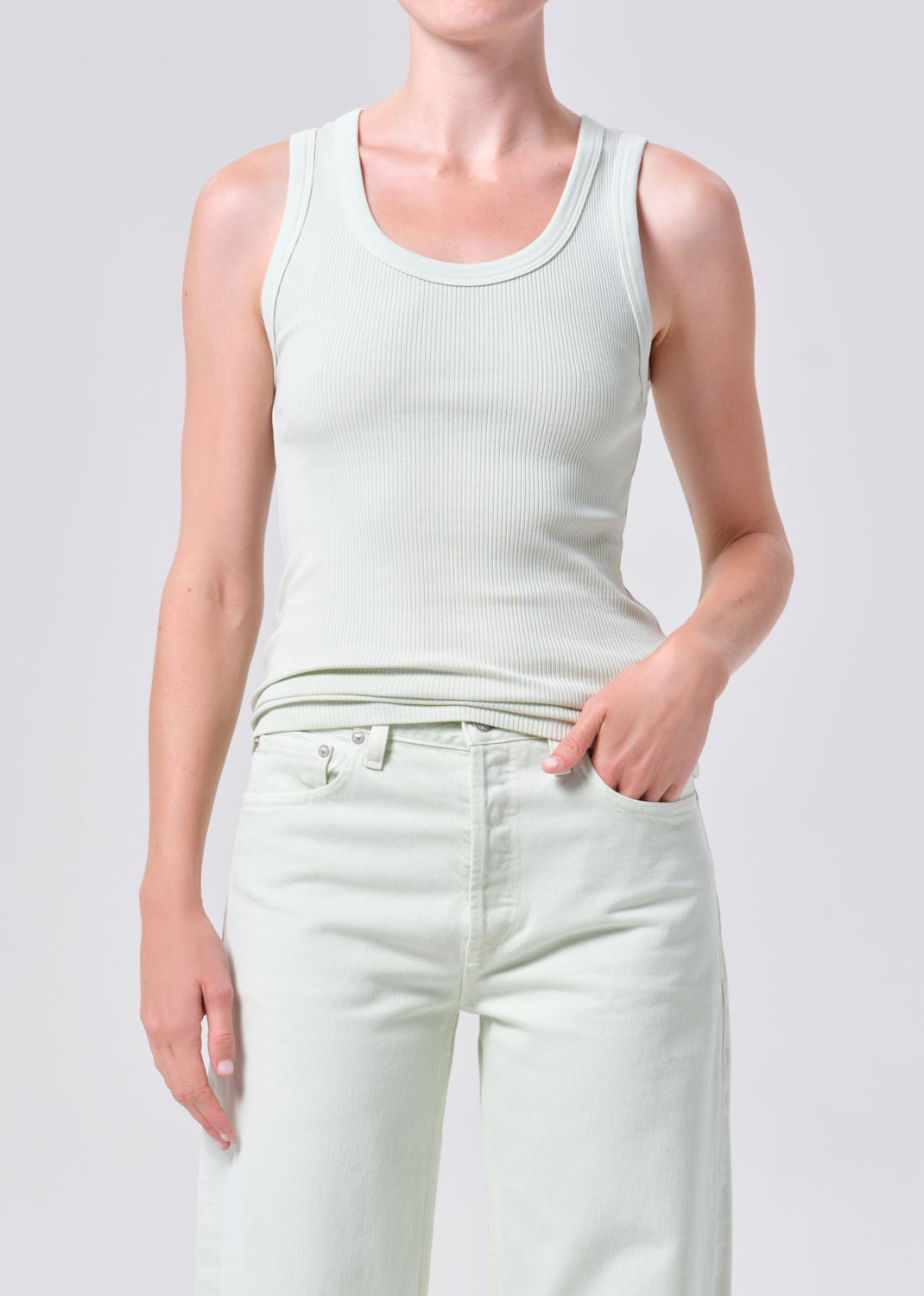 Person wearing a light green tank top and white pants on a plain background