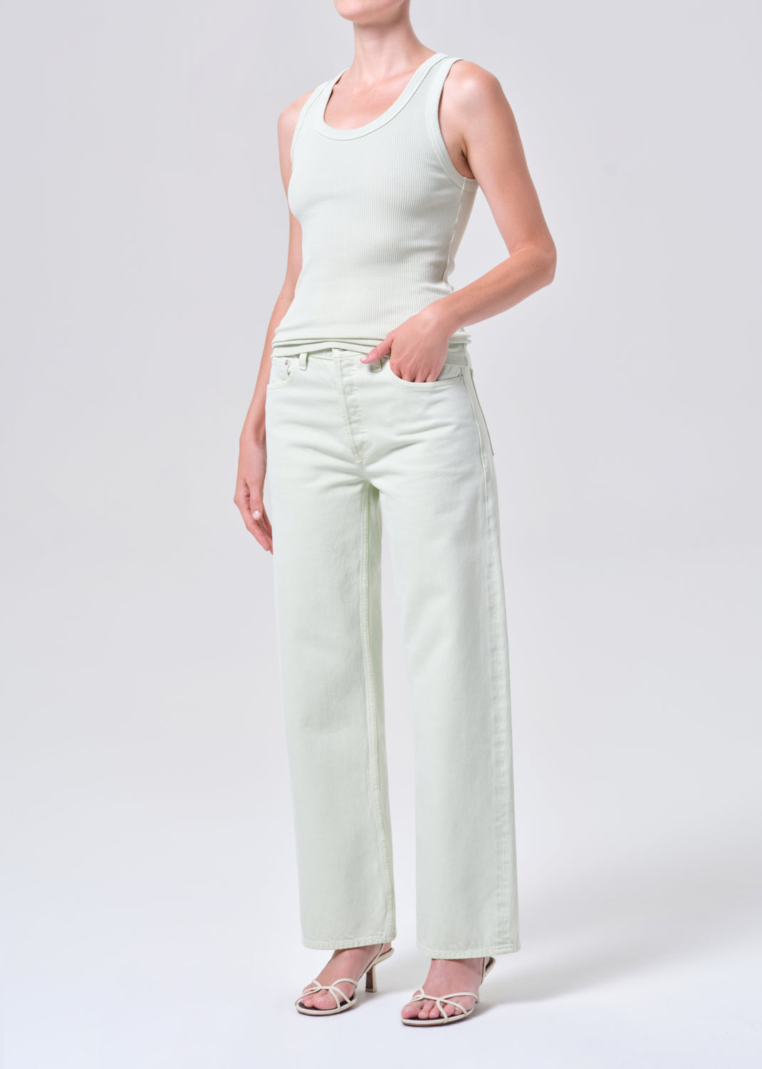 Person wearing a light green sleeveless top and wide-leg pants on a white background