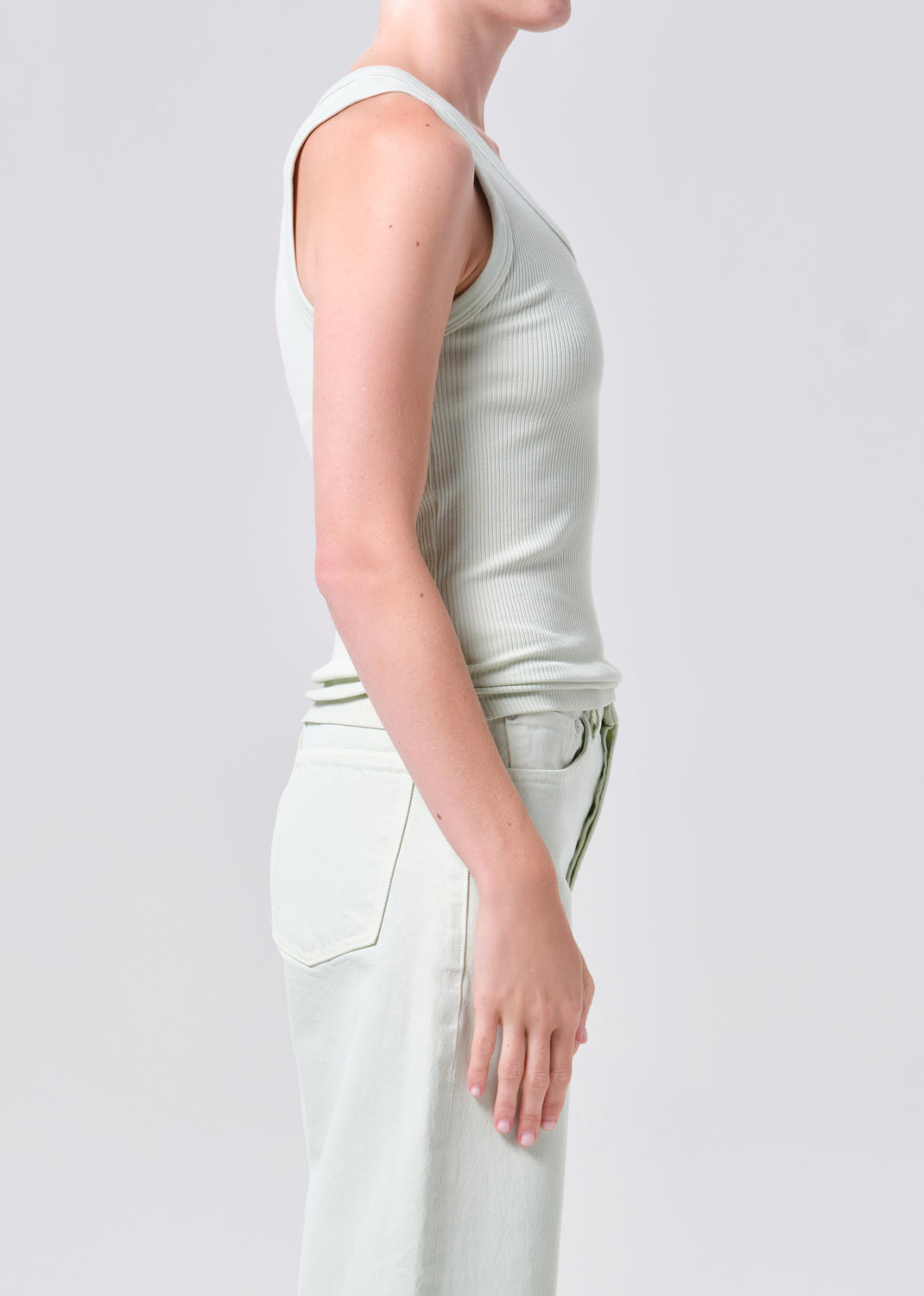 Person wearing a light green sleeveless top and white pants on a plain background