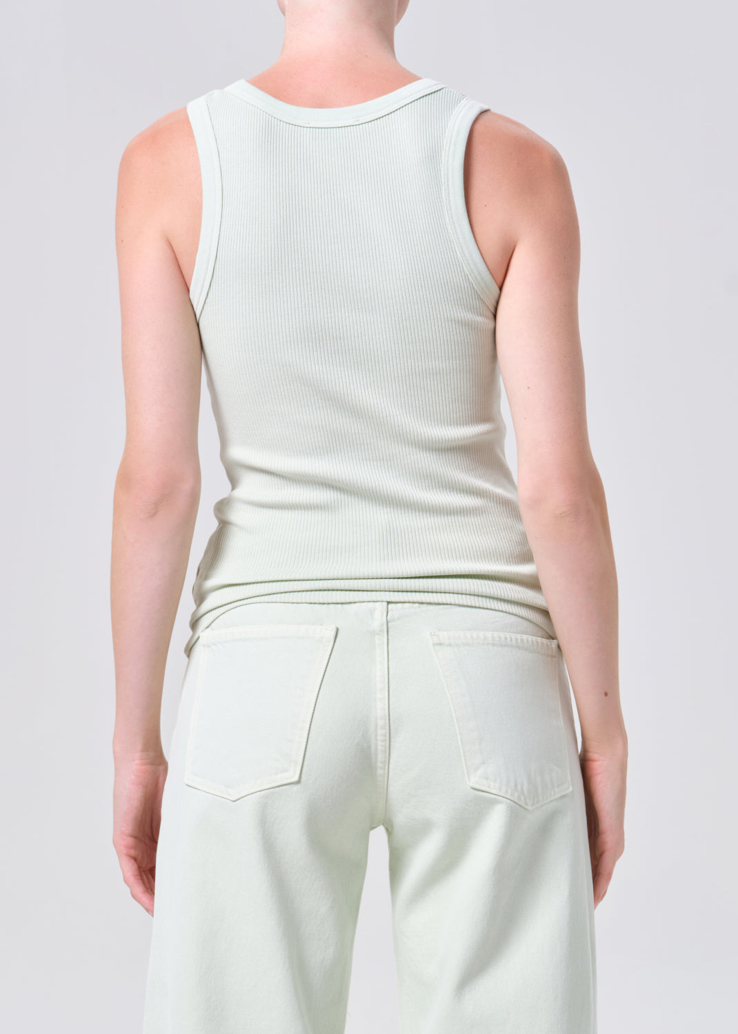 Person wearing a light-colored sleeveless top and pants on a plain background