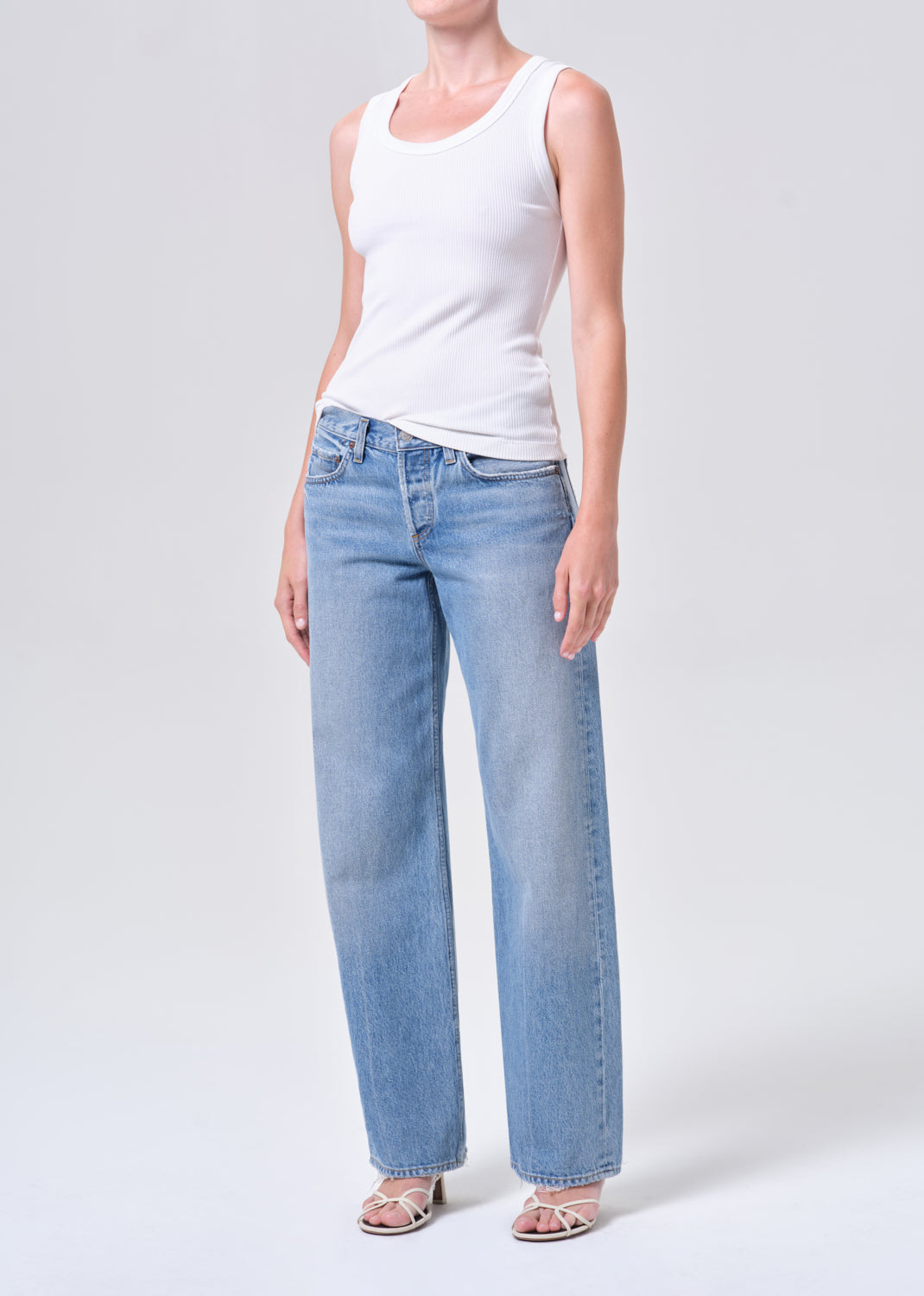 Person wearing a white tank top and light blue jeans on a white background