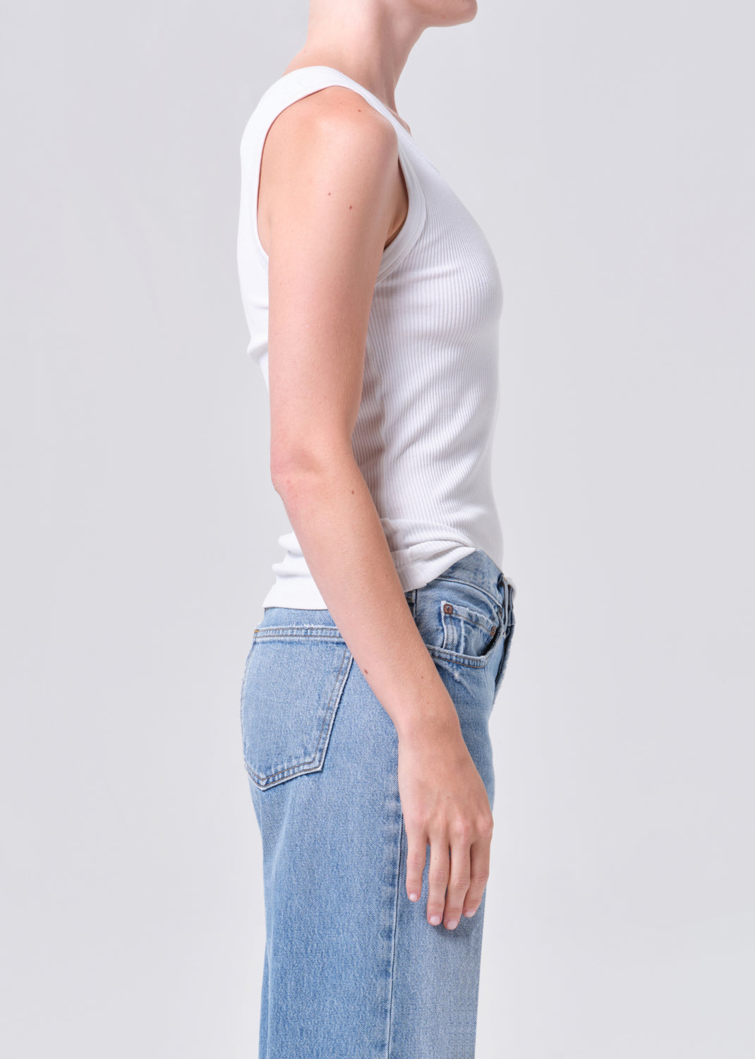 Person wearing a white tank top and blue jeans on a plain background
