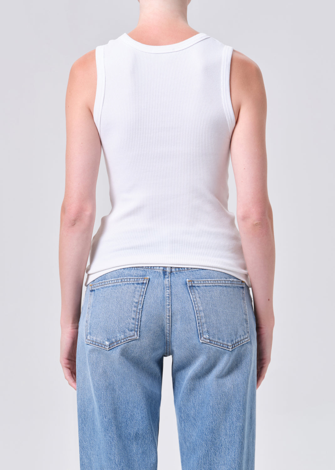 Person wearing a white tank top and light blue jeans on a plain background