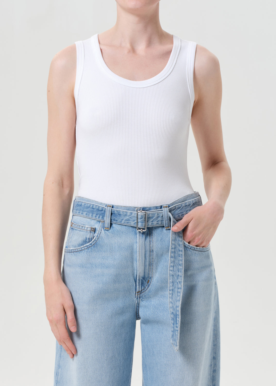 Person wearing a white tank top and light blue jeans on a plain background