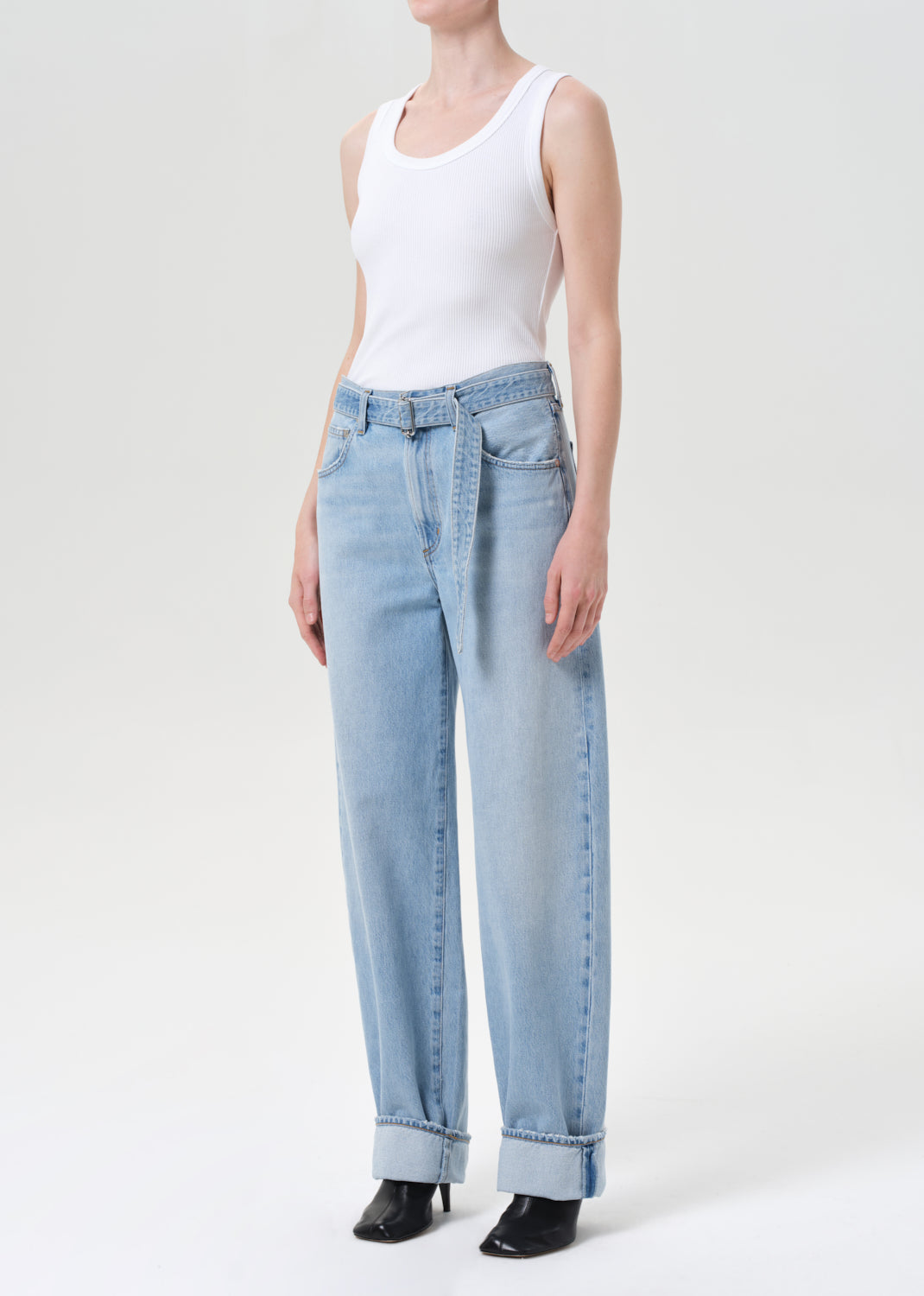 Person wearing light blue jeans and a white tank top on a white background