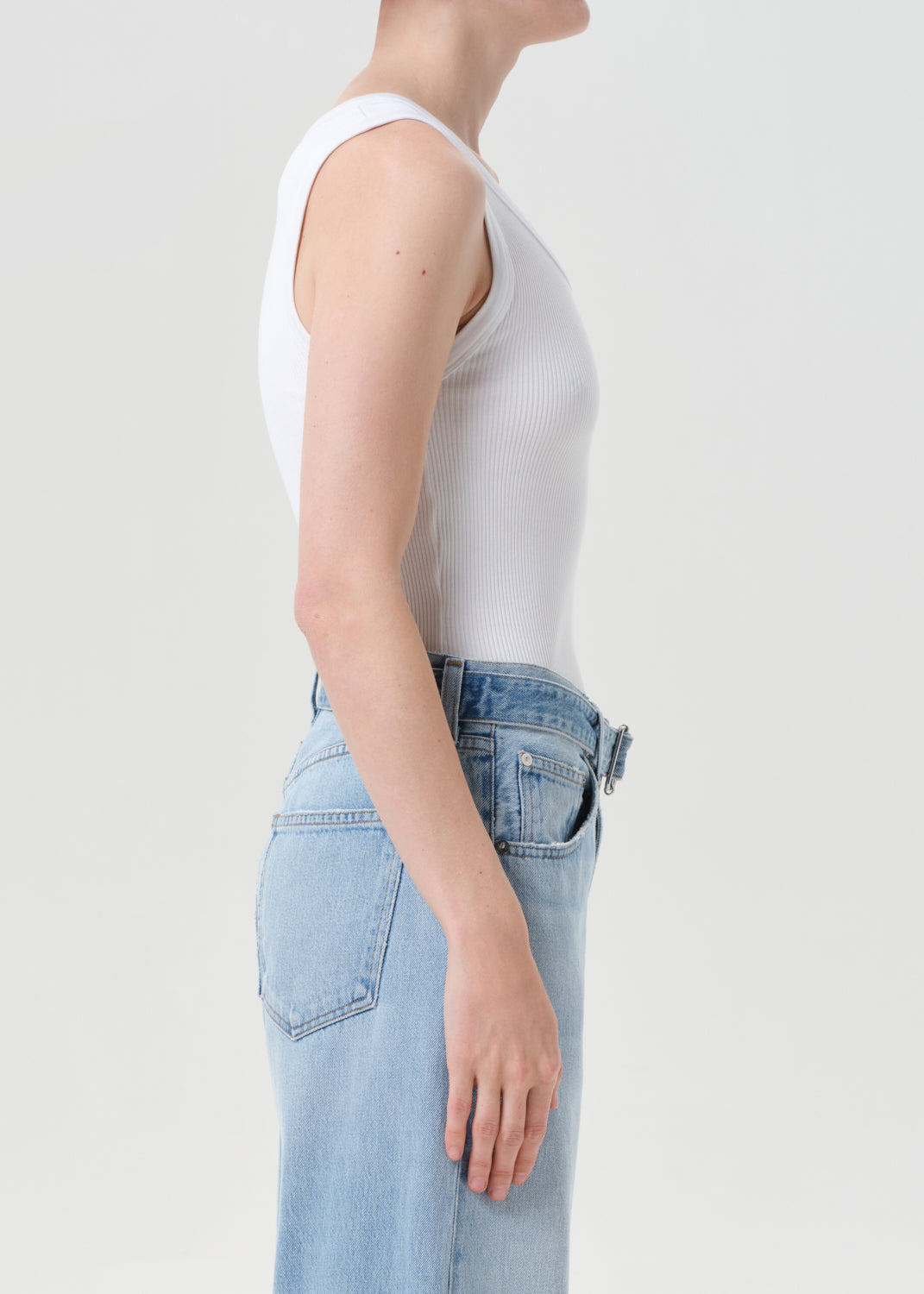 Person wearing a white tank top and light blue jeans on a plain background