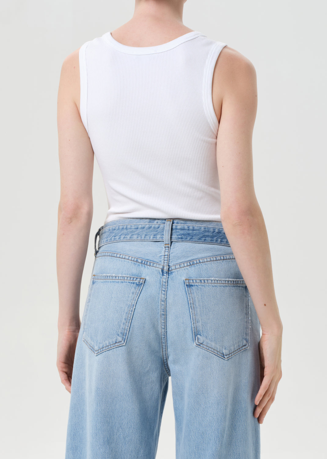 Person wearing a white tank top and light blue jeans on a plain background