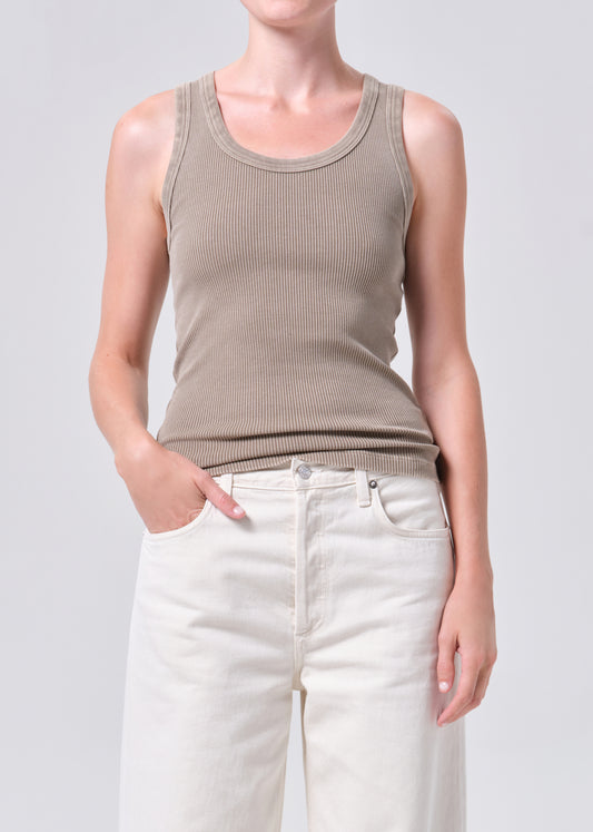 Person wearing a beige tank top and white pants on a plain background