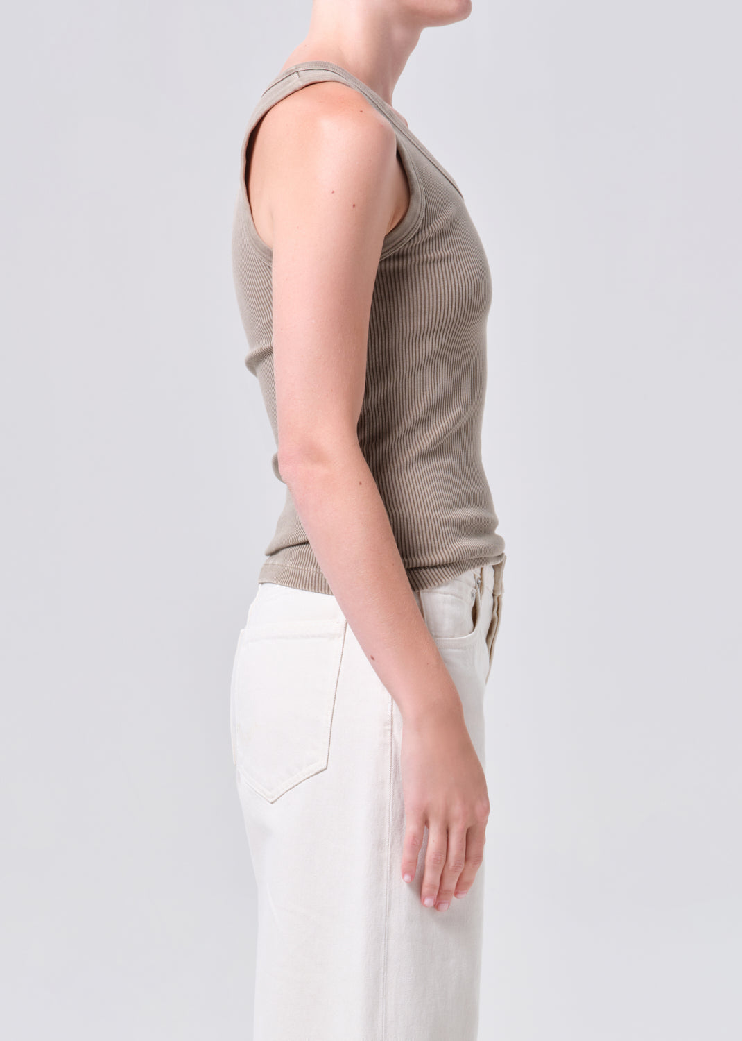 Person wearing a brown sleeveless top and white pants on a light gray background