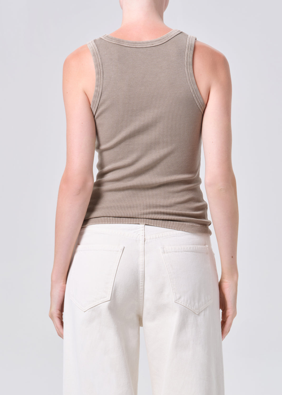 Person wearing a beige ribbed tank top and white pants on a light gray background