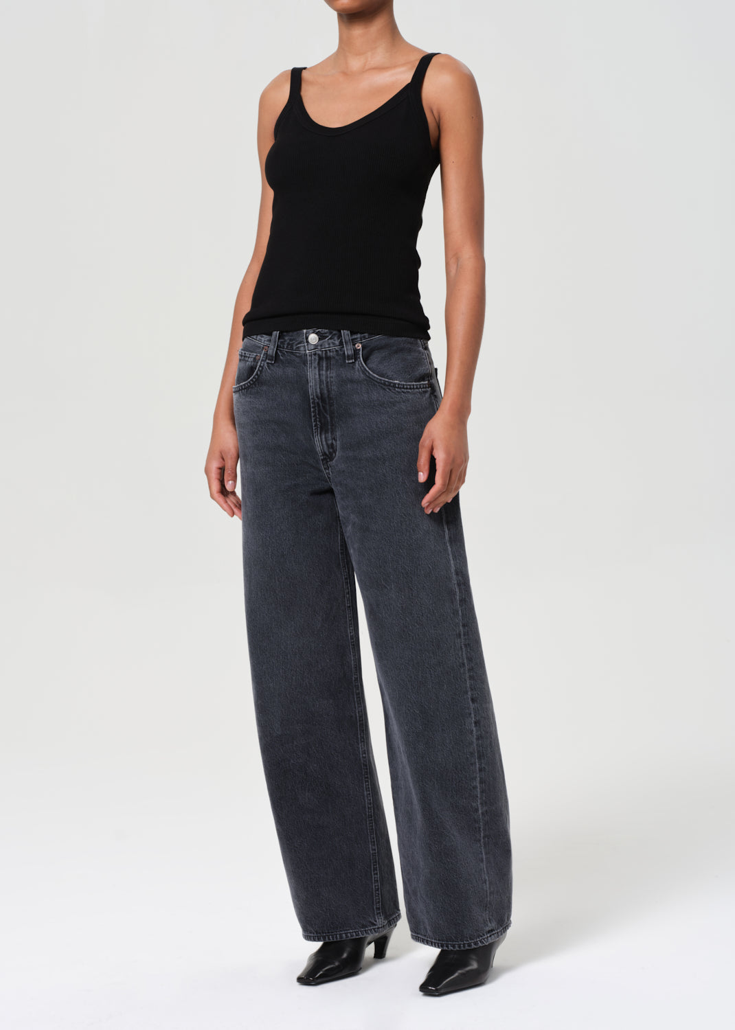 Person wearing a black tank top and dark blue jeans on a white background