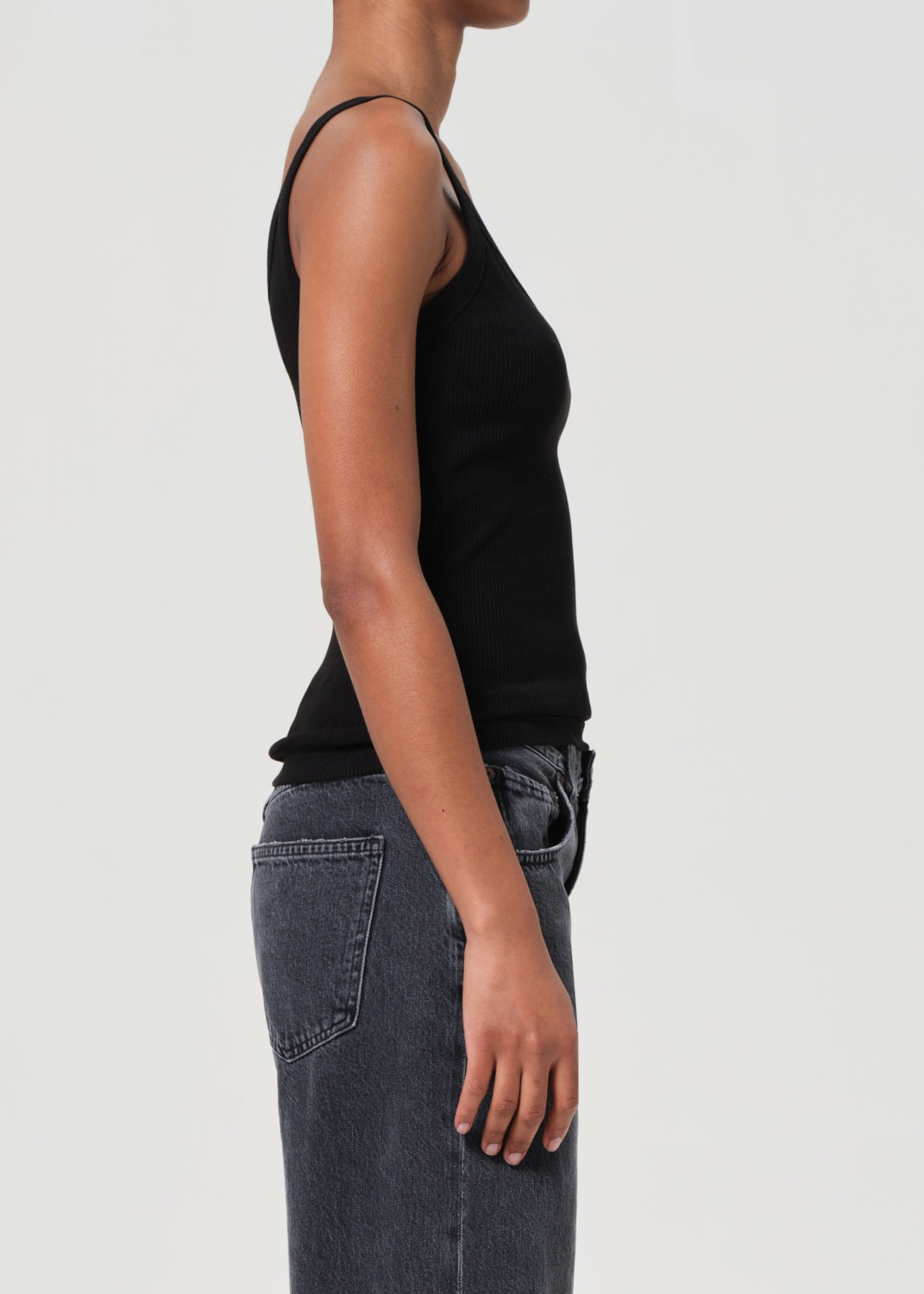 Person wearing a black tank top and blue jeans on a light gray background