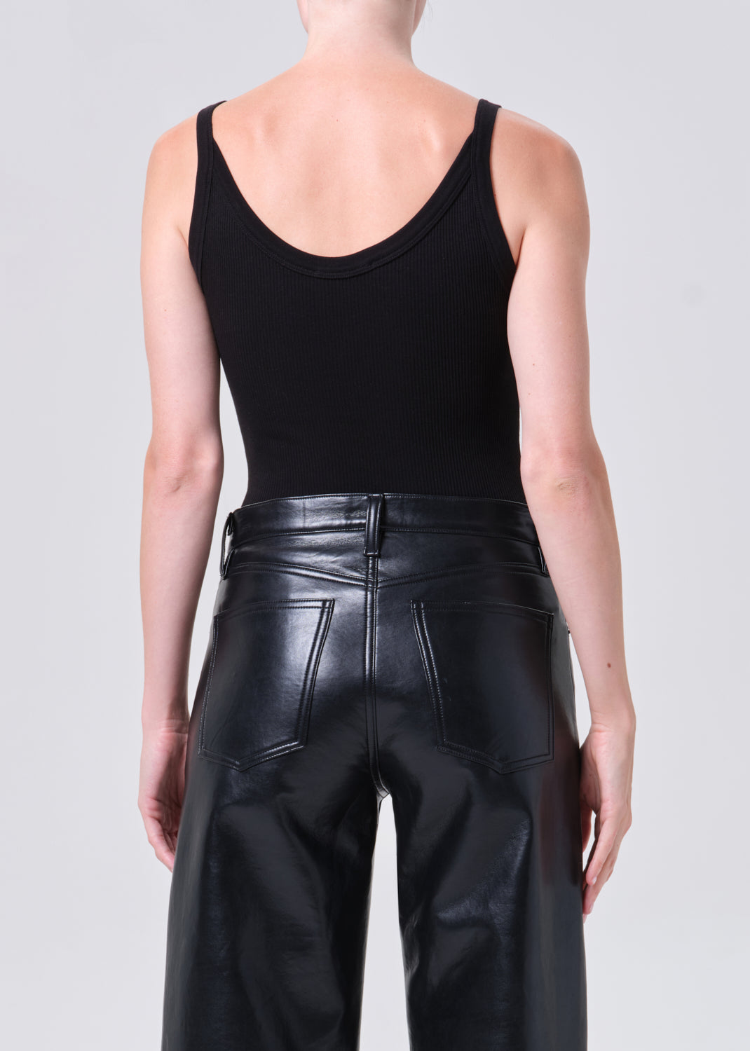Person wearing a black tank top and black leather pants on a plain background