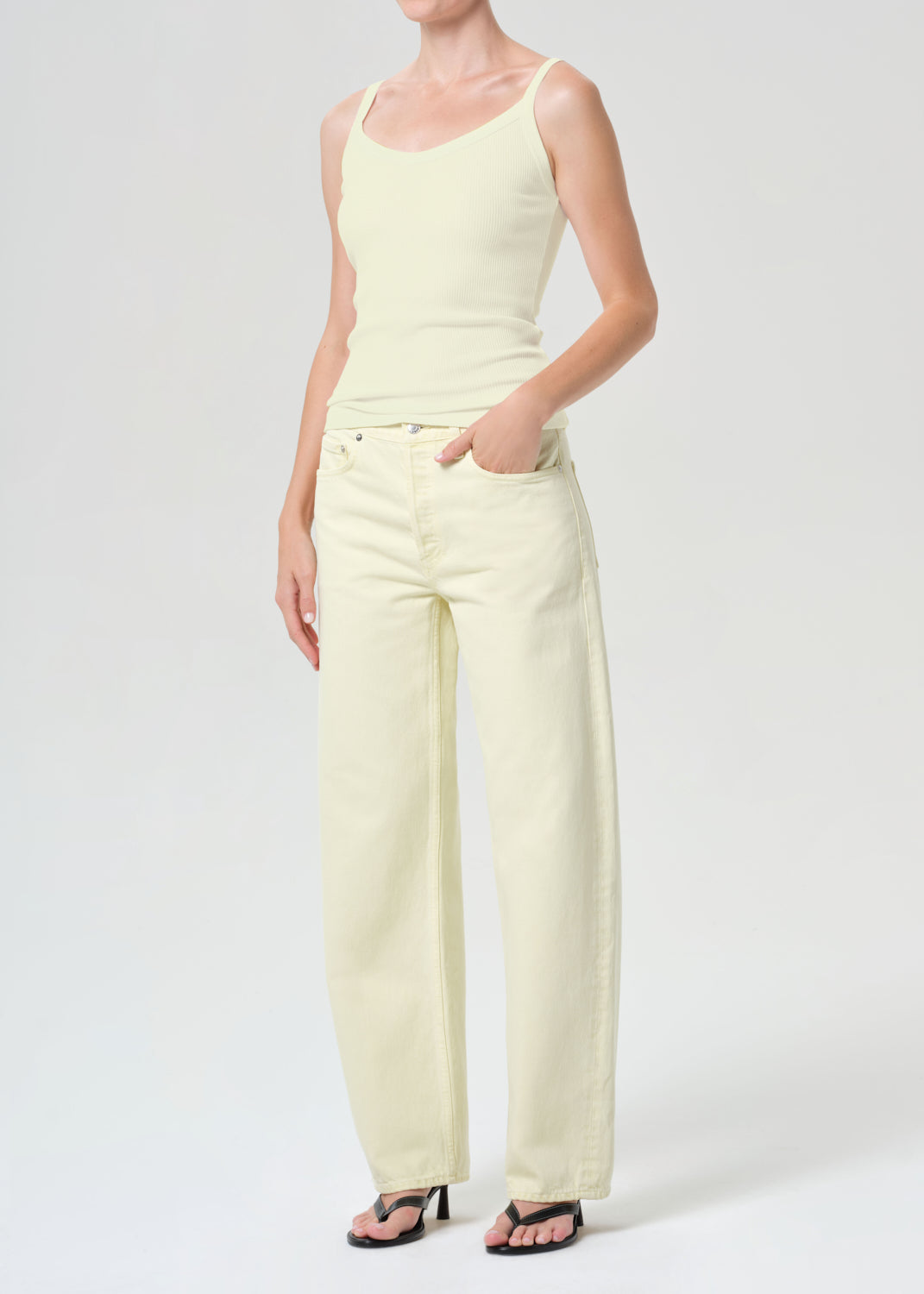 Person wearing a light yellow sleeveless top and wide-leg pants on a white background