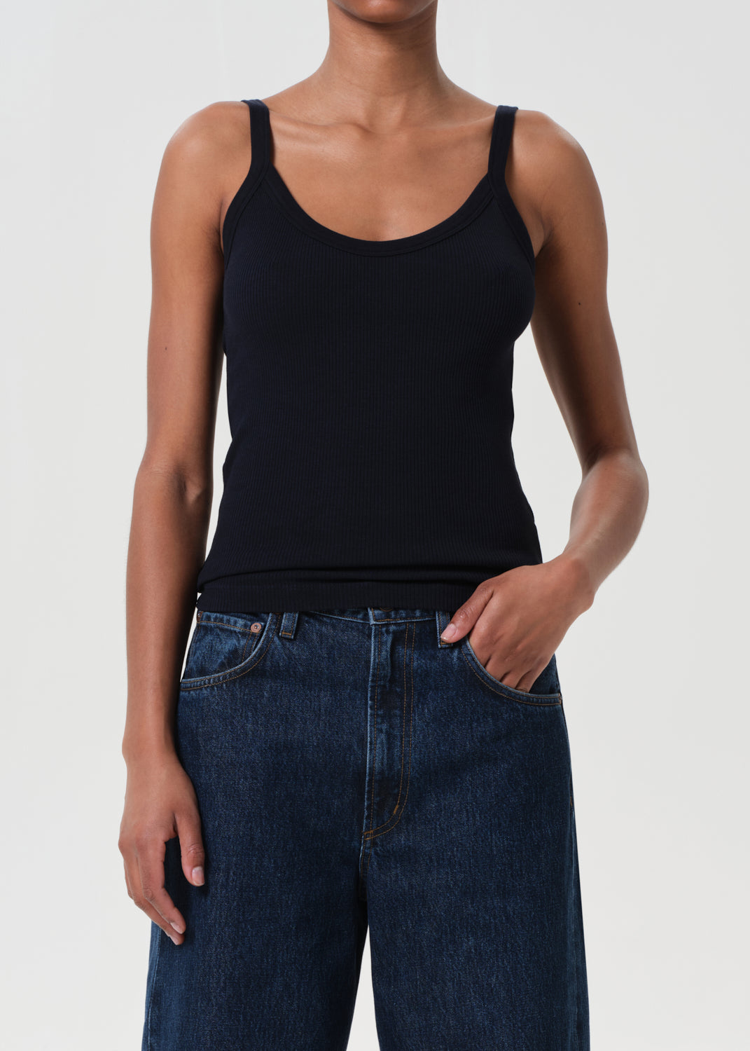 Person wearing a black tank top and blue jeans on a plain background