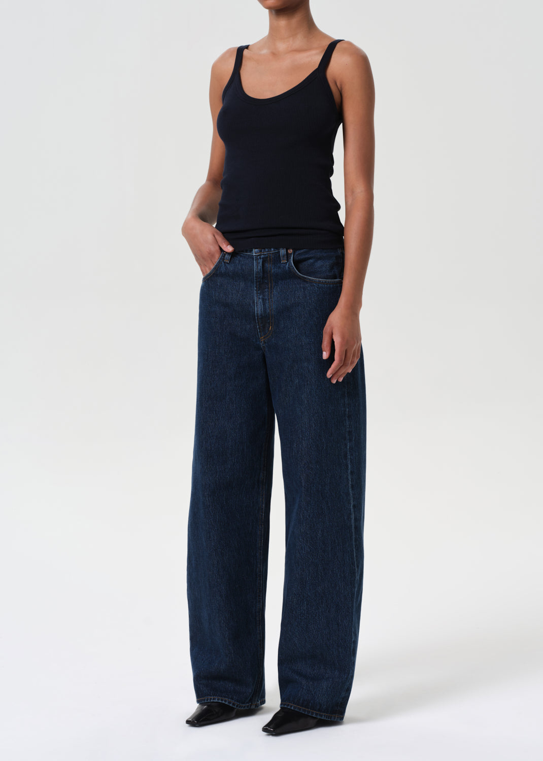 Person wearing a black tank top and dark blue jeans on a white background