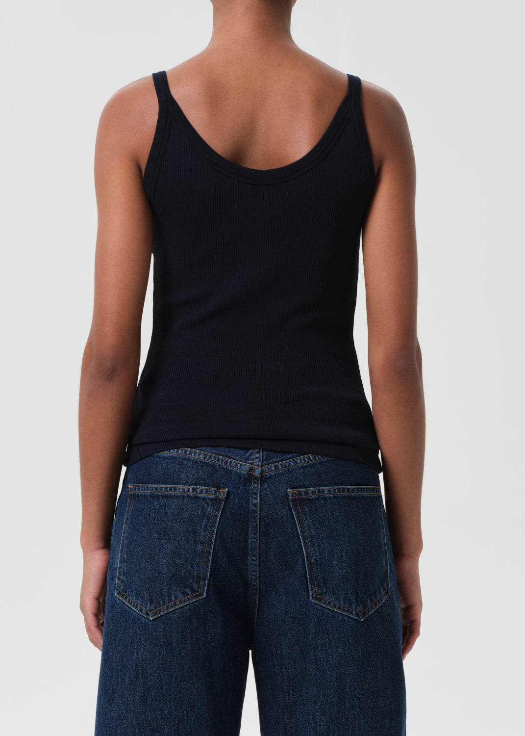 Person wearing a black tank top and blue jeans on a white background