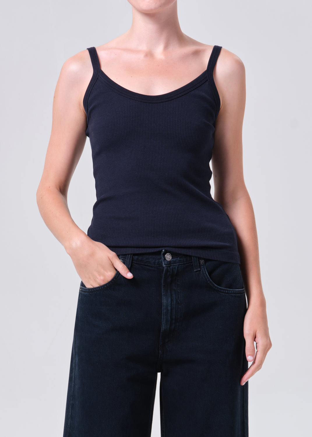 Person wearing a black tank top and dark jeans on a light gray background