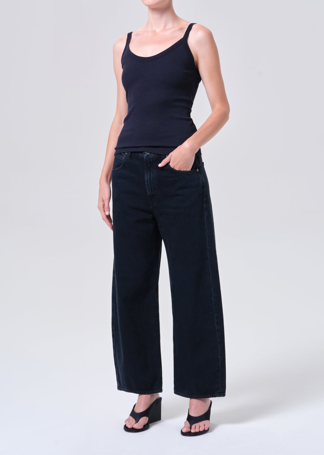 Person wearing a black tank top and wide-leg jeans on a white background