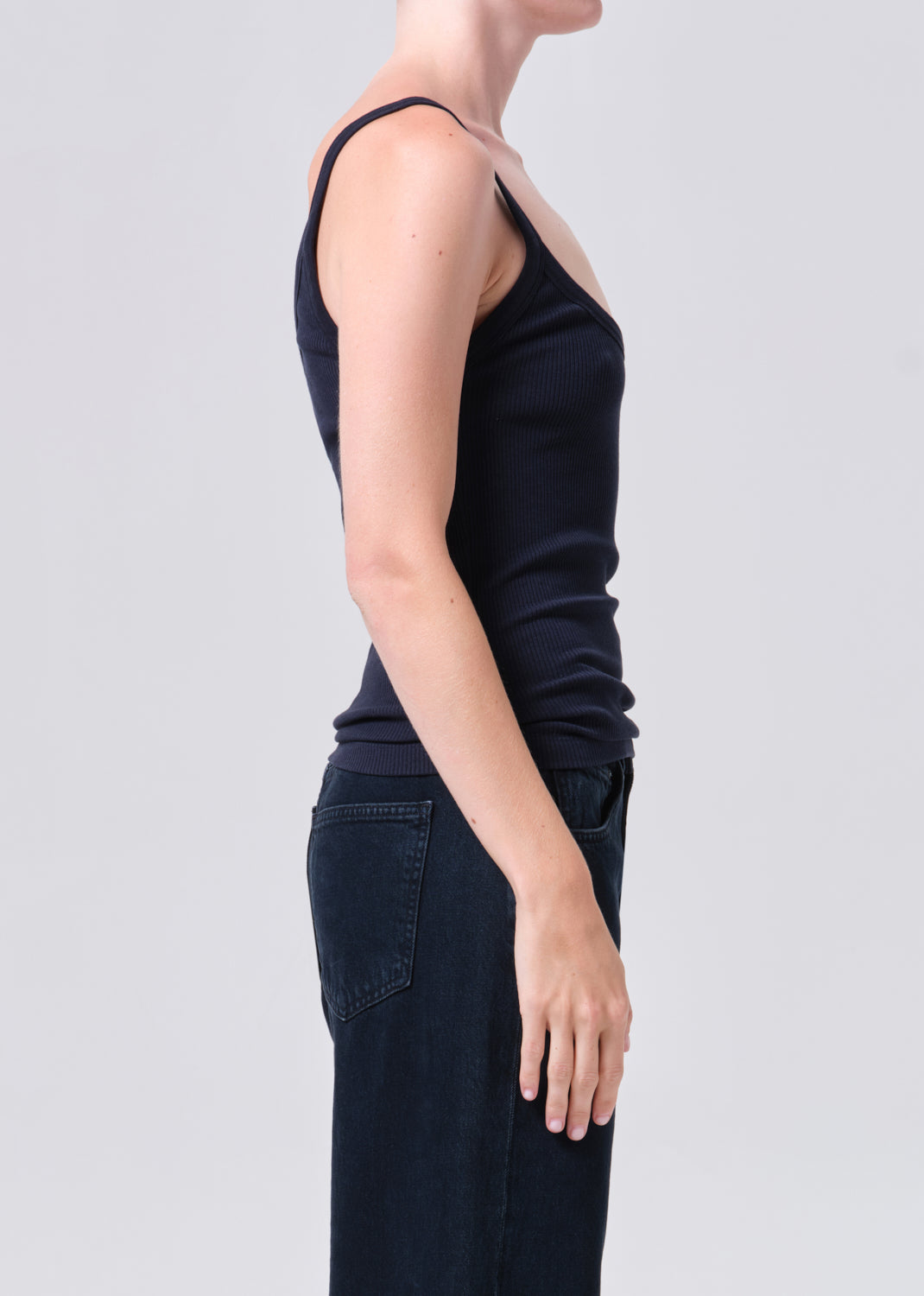 Person wearing a black tank top and dark pants on a light gray background