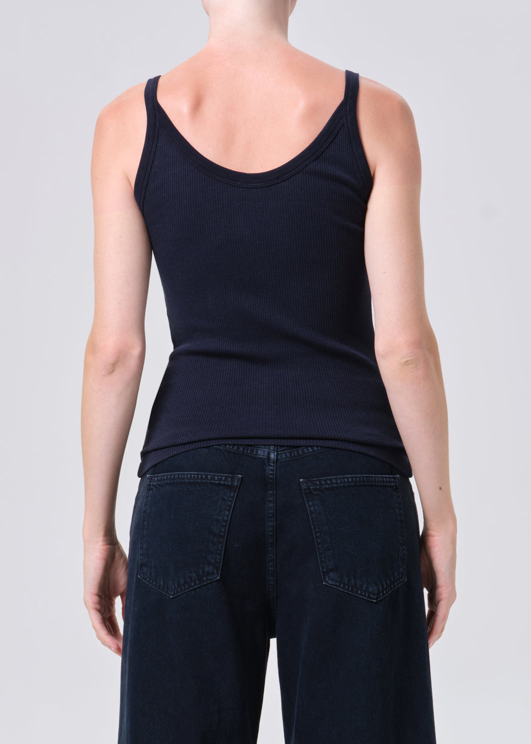 Person wearing a black tank top and dark jeans on a plain background