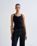 A model wearing a black ribbed knit camisole tank top and dark blue jeans, standing against a light gray studio background.