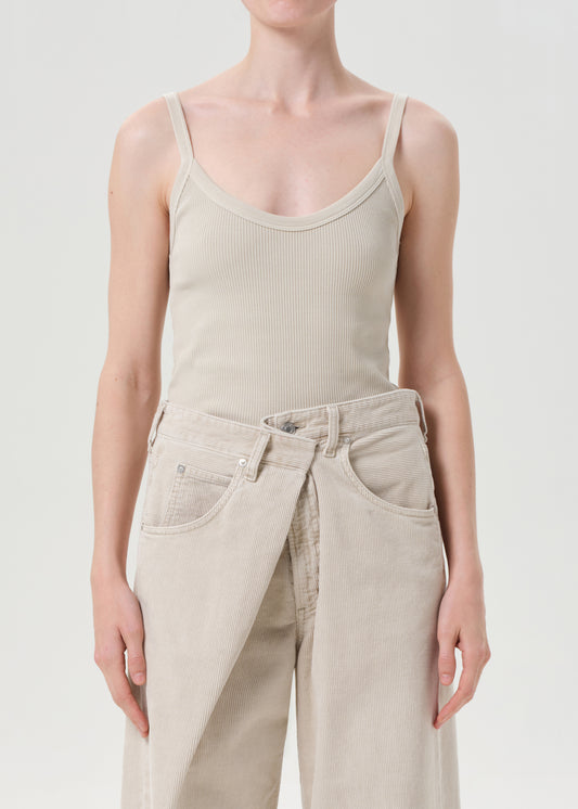 Person wearing a beige ribbed tank top and pants on a light gray background