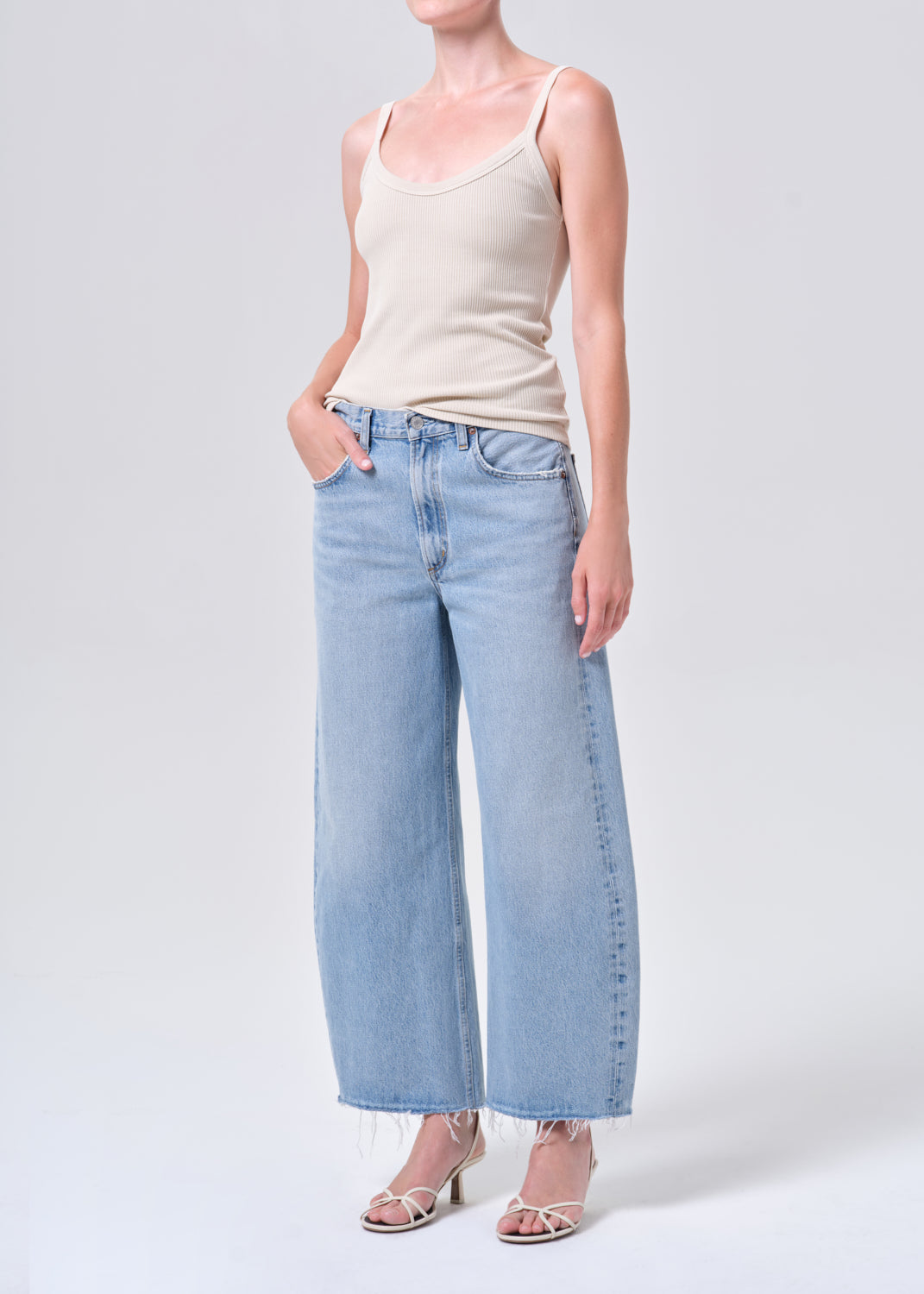 Person wearing a beige tank top and light blue jeans on a white background