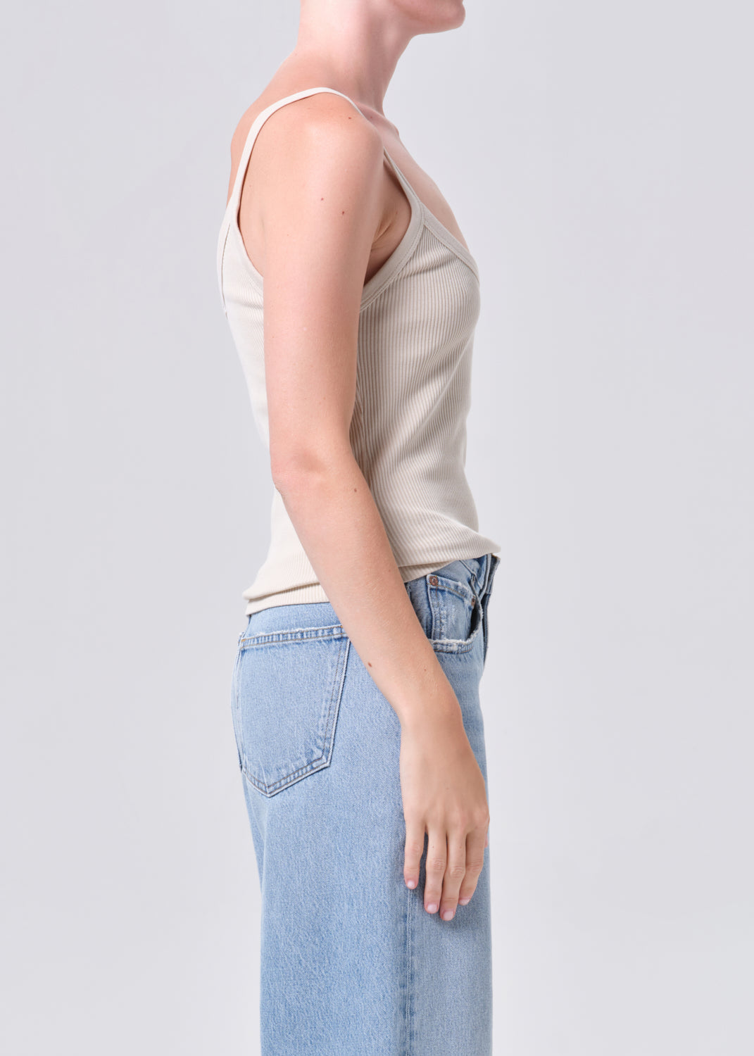 Person wearing a beige tank top and light blue jeans on a plain background